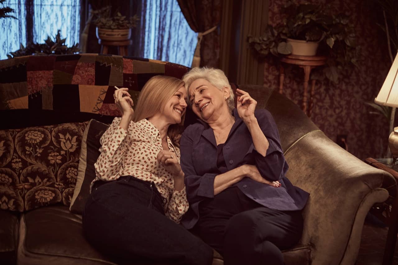 Laura Linney e Olympia Dukakis sono sedute vicine su divano. Si guardano e ridono. Hanno entrambe in mano una sigaretta. 